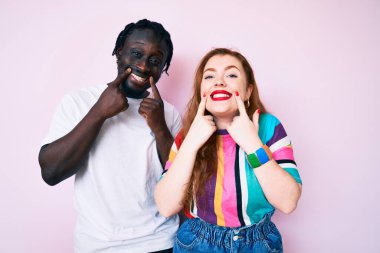 Irklar arası çift gündelik kıyafetler giyer ağzı açık gülümserler, parmakları işaret eder ve neşeli gülümsemeye zorlarlar. 