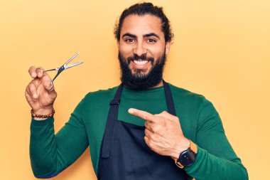 Berber önlüklü genç Arap adam mutlu bir şekilde el ve parmağıyla işaret ediyor. 