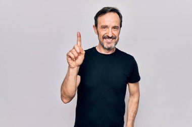 İzole edilmiş beyaz arka planda dikilen siyah tişörtlü orta yaşlı bir adam bir fikir veya soruyla gülümsüyor ve mutlu bir yüzle işaret ediyor.