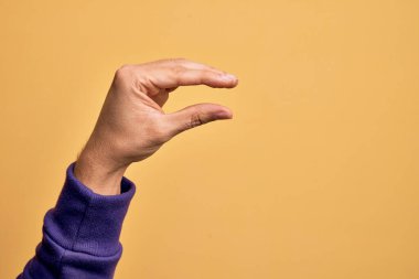 İzole edilmiş sarı arka plan üzerinde parmaklarını gösteren beyaz bir adamın eli. Görünmez bir şeyi alıp, parmaklarıyla uzayı gösteren bir nesneyi tutuyor.