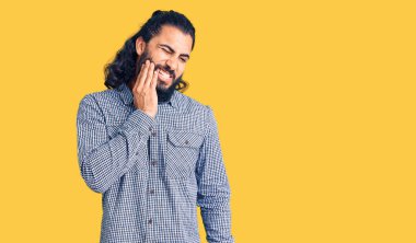 Sıradan kıyafetler giyen genç bir Arap diş ağrısı ya da diş hastalığından dolayı acı dolu bir ifadeyle ağıza dokunuyor. dişçi 