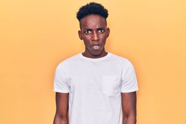 Şok olmuş gibi giyinmiş, kuşkucu ve iğneleyici bakışları olan, ağzı açık kalmış genç Afro-Amerikan bir adam. 