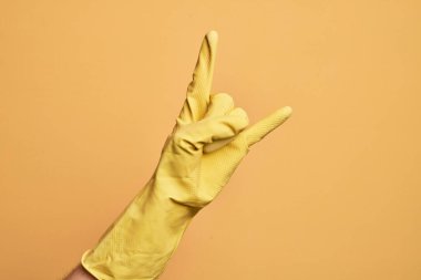 İzole edilmiş sarı arka planda, rock 'n roll sembolü taşıyan, müstehcen boynuzlar gösteren temiz eldivenli beyaz bir gencin eli.