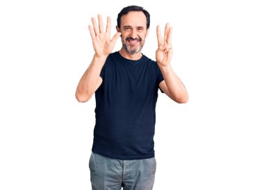 Orta yaşlı yakışıklı bir adam gündelik tişört giyer ve 8 numaralı parmaklarıyla işaret ederken kendinden emin ve mutlu bir şekilde gülümser.. 