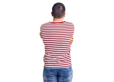 Çizgili kazak giyen genç yakışıklı bir adam kendine sarılıyor, mutlu ve pozitif. Sevgi ve özgüven. 