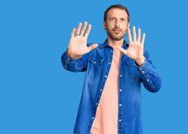 Sıradan kıyafetler giyen genç yakışıklı adam korku ifadesinden korkmuş ve dehşete düşmüş. El hareketlerini durdur, şok içinde bağır. panik konsepti. 