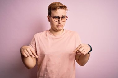 Genç, yakışıklı, günlük tişört giyen, pembe arka planda duran üzgün ve üzgün görünen mutsuz ve depresif yönünü gösteren bir adam..