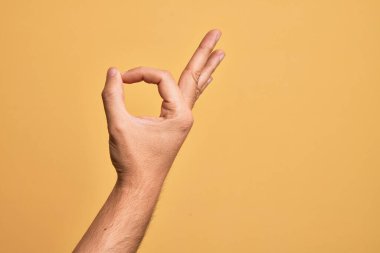 İzole edilmiş sarı arka plan üzerinde parmaklarını gösteren beyaz bir gencin eli işaret ediyor. Onaylama ifadesi parmaklarıyla iyi bir sembol oluşturuyor.