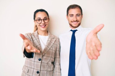 İş elbiseleri giymiş güzel bir çift neşeli bir gülümseme içinde avuç içi yardım ve kabul vaadinde bulunuyor.. 