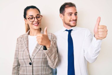 İş kıyafetleri giymiş güzel bir çift gururlu görünüyor, gülümsüyor ve baş parmaklarını kaldırıyor. 