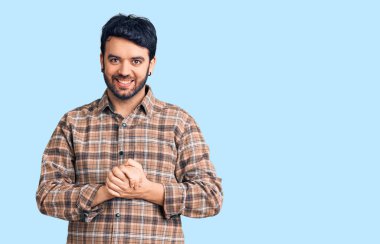 Latin asıllı genç adam ellerinin birleştiği günlük kıyafetler giyiyor ve gülümseyerek gevşemiş ve neşeli gülümsüyor. Başarı ve iyimserlik 
