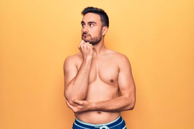 Sakallı, kolsuz tişörtlü genç yakışıklı sarı arka planda duran ciddi yüzlü eli çeneli soruyu düşünen kafa karıştırıcı bir fikir.