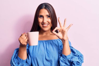 Genç, güzel esmer kadın kahve fincanı içiyor parmaklarıyla imza atıyor, gülümseyerek mükemmel bir sembol oluşturuyor. 