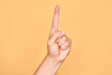 İzole edilmiş sarı arka planda parmaklarını gösteren beyaz bir gencin eli işaret parmağı kullanarak bir numarayı sayıyor, fikir ve anlayış gösteriyor.
