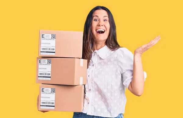 Young Beautiful Brunette Woman Holding Delivery Cardboard Package Celebrating Victory — Stock Photo, Image
