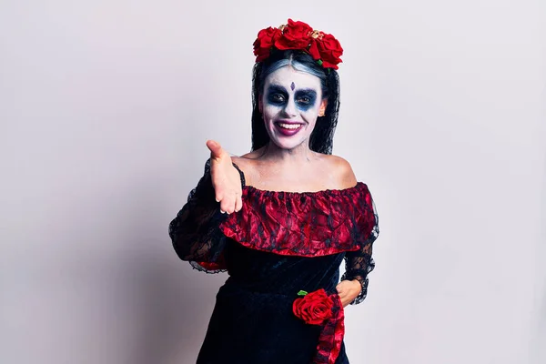 Young woman wearing mexican day of the dead makeup smiling friendly offering handshake as greeting and welcoming. successful business.