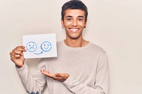 Young african amercian man holding sad to happy emotion paper looking positive and happy standing and smiling with a confident smile showing teeth