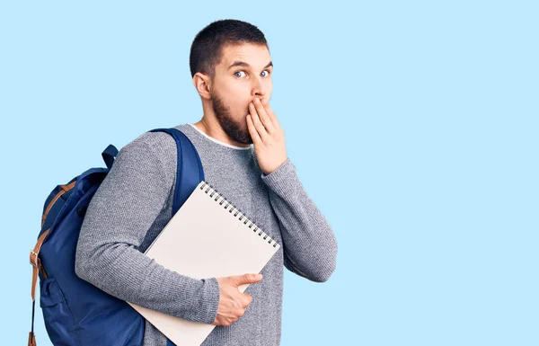 Joven Hombre Guapo Con Mochila Estudiante Sosteniendo Cuaderno Cubriendo Boca —  Fotos de Stock