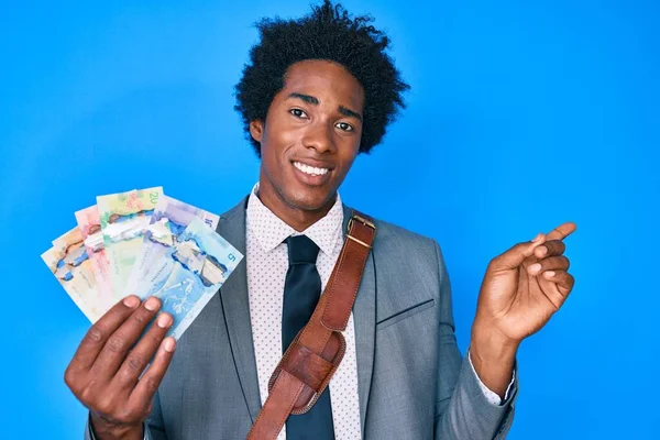 Handsome african american business man with afro hair holding canadian dollars smiling happy pointing with hand and finger to the side