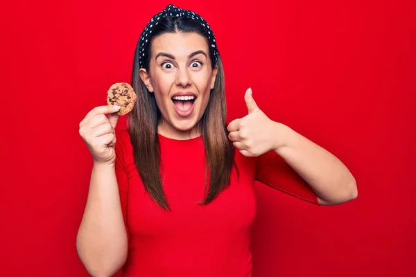 Joven Hermosa Morena Sosteniendo Dulce Galleta Chocolate Sobre Fondo Rojo —  Fotos de Stock