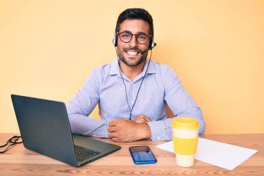 Çağrı merkezindeki operatör kulaklığı takmış genç İspanyol adam olumlu ve mutlu görünüyor. Kendine güvenen bir gülümsemeyle dişlerini gösteriyor. 