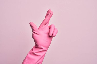 İzole edilmiş pembe arka plan üzerinde temizleme eldiveni olan beyaz bir gencin eli. Parmakları çapraz, batıl inançlar ve şanslı bir jest, şanslı ve umut ifadesi.