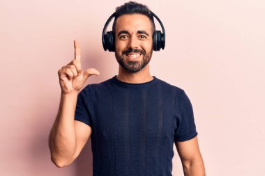 Genç İspanyol adam müzik dinlerken kulaklık takıyor ve başarılı bir fikri işaret ediyor. Heyecanlı ve mutlu. Bir numara.. 