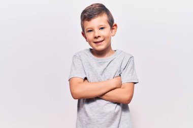 Sıradan kıyafetler giyen sevimli sarışın çocuk kollarını kavuşturup kameraya bakarken gülümsüyor. pozitif kişi. 