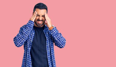 Latin asıllı genç bir adam elleri kafasında günlük kıyafetler giyiyor, stres yüzünden baş ağrısı çekiyor. migren ağrısı. 