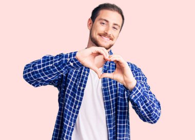 Genç, yakışıklı, beyaz, sıradan kıyafetler giyen, aşık gülümseyen, elleriyle kalp sembolü yapan bir adam. romantik kavram. 