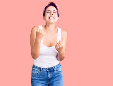 Pembe saçlı, mutlu ve heyecanlı genç bir kadın kolları havada, gülümseyen ve başarı için bağıran bir jest yapıyor. kutlama konsepti. 