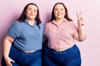 Genç ve cüsseli ikizler gündelik giysiler giyip iki numarayı gösteriyorlar ve mutlu bir şekilde gülümsüyorlar.. 