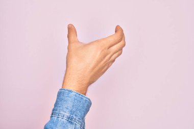 Kafkasyalı genç adam parmaklarını pembe arka planda gösteriyor. Görünmez bir nesne tutuyor, eli boş, kesiyor ve kapıyor.