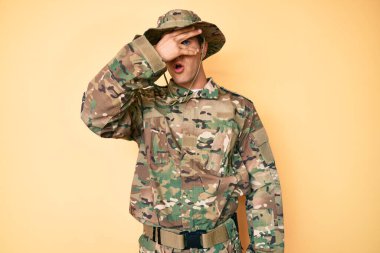 Kamuflaj üniforması giyen genç yakışıklı adam şok içinde yüzünü ve gözlerini kapayarak utangaç ifadesiyle parmaklarının arasından bakıyor.. 