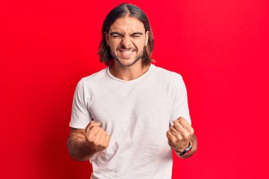 Gündelik kıyafetler giyen, mutlu ve heyecanlı genç bir adam kollarını kaldırmış, gülümseyen ve başarı için çığlık atan kazanan bir jest yapıyor. kutlama konsepti. 