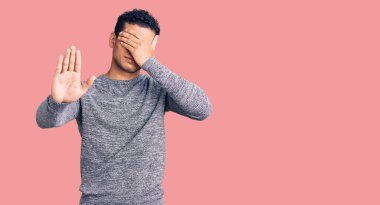 İspanyol asıllı yakışıklı genç adam, gündelik kazak giyip elleriyle gözlerini kapatıyor ve üzgün ve korku ifadeleriyle jestleri durduruyor. utangaç ve olumsuz kavram. 