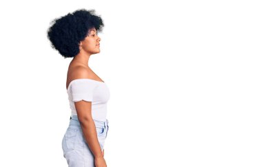 Afro-Amerikalı genç bir kız, günlük giysiler giymiş, rahat bir görünüm takınıyor, doğal bir yüz ifadesi ve kendine güvenen bir gülümsemeyle poz veriyor.. 