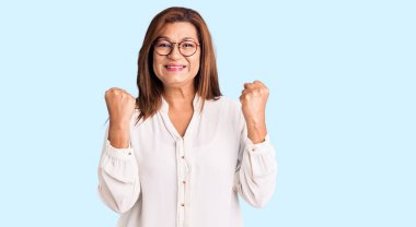 Orta yaşlı, gündelik kıyafetler ve gözlük takan Latin bir kadın kollarını kaldırarak ve açık gözlerle başarıyı kutluyor. Kazanan konsept. 