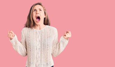 Genç ve güzel sarışın kadın, gündelik kazak giyip deli gibi bağırıyor ve agresif bir ifadeyle bağırıyor ve kollarını kaldırıyor. hüsran kavramı. 