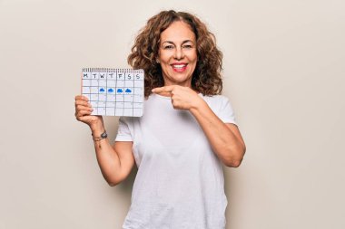 Orta yaşlı güzel bir kadın, elinde iklim takvimi tutarken bulutlu ve yağmurlu havanın mutlu bir şekilde gülümsediğini gösteriyor.