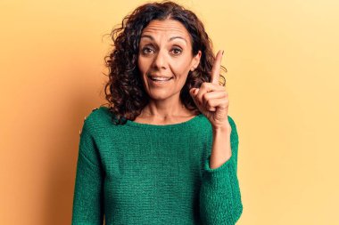 Orta yaşlı güzel bir kadın bir fikir veya soruyla gülümseyen bir süveter giyer ve mutlu bir yüzle işaret eder. 