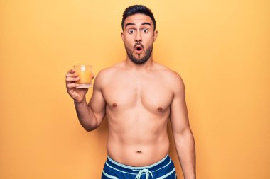 Tatilde sakallı, mayo giyen, bir bardak portakal suyu içen, korkmuş ve ağzı açık, şaşırmış genç bir adam.