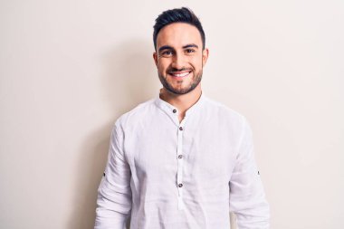 Sakallı, sıradan tişörtlü, beyaz arka planda mutlu ve havalı bir gülümsemesi olan genç yakışıklı bir adam. Şanslı kişi..