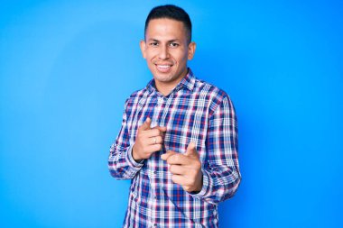 Genç, yakışıklı, gündelik kıyafetler giyen, mutlu ve komik yüzlü, kamerayı işaret eden Latin adam. iyi enerji ve titreşimler. 