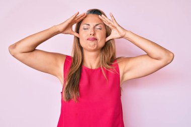 Orta yaşlı İspanyol kadın, elleri kafasında günlük kıyafetler giyiyor, stres yüzünden baş ağrısı çekiyor. migren ağrısı. 