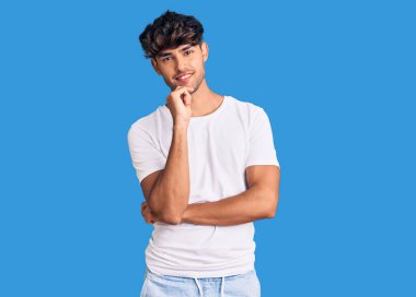 Gündelik kıyafetler giyen genç İspanyol adam kameraya bakıyor kollarını kavuşturup gülümseyerek ve çenesini kaldırarak. Olumlu düşünmek. 