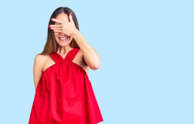 Güzel, esmer, sıradan kıyafetler giyen, gülümseyen ve elleri yüzünde, şaşırtmak için gözlerini kapatan genç bir kadın. kör kavram. 