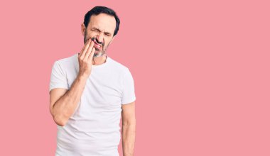 Orta yaşlı yakışıklı bir adam diş ağrısı ya da diş hastalığından dolayı ağzıyla dokunan sıradan tişörtler giyiyor. dişçi 