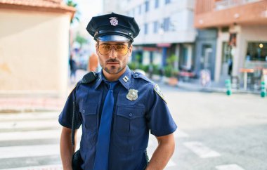 Polis üniforması giyen genç, yakışıklı İspanyol polis. Kasaba caddesinde ciddi bir ifadeyle dikiliyorsun..