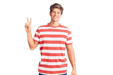 Gündelik kıyafetler giyen genç yakışıklı adam iki numarayı gösterip işaret ederken kendinden emin ve mutlu bir şekilde gülümsüyor.. 